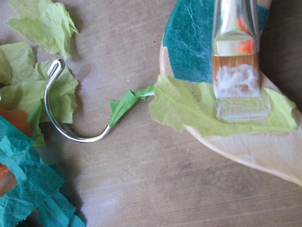 Working quickly, pick up a piece of tissue with the brush and place it on the glued section of the hanger. Gently brush additional medium onto the piece to attach and smooth. Working quickly, pick up a piece of tissue with the brush and place it on the glued section of the hanger. Gently brush additional medium onto the piece to attach and smooth.